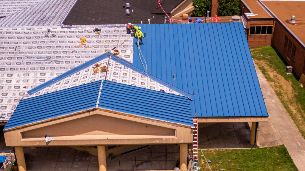 Professional roofers installing standing seam metal roofing on a commercial building